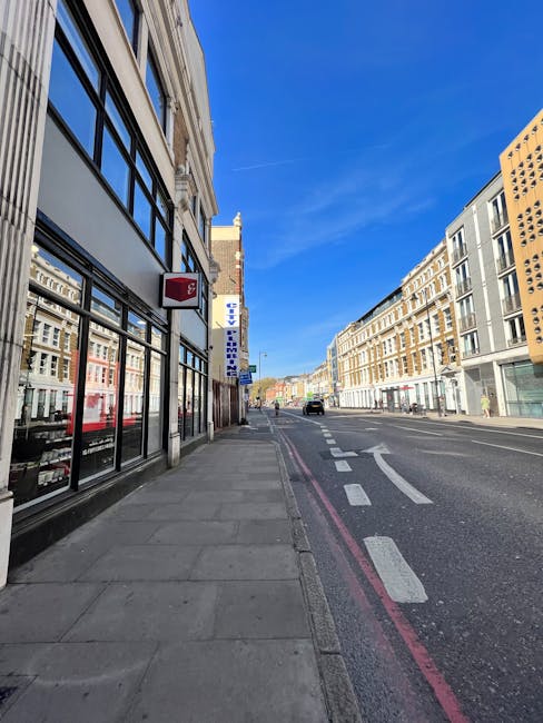 A busy urban street scene in the City of London with modern and historic buildings lining the road, featuring a temporary road closure with traffic barriers, warning signs, and cones restricting vehic